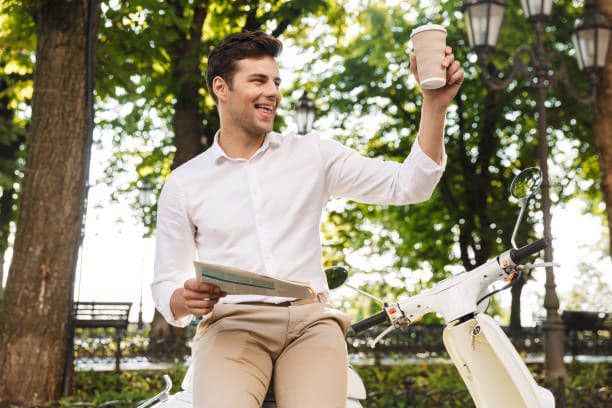 Pria yang duduk di sepeda motor dengan membaca koran dan minum kopi (istockphoto.com/DeanDrobot)