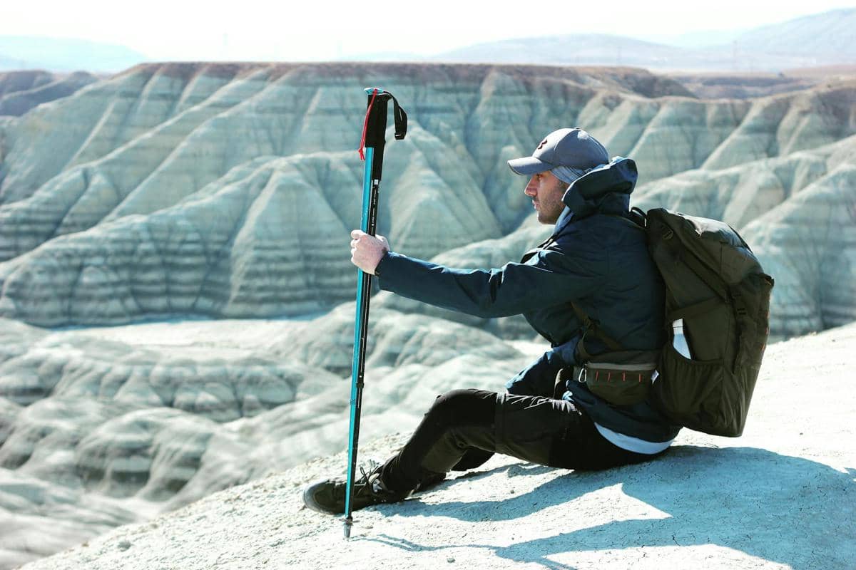 seorang pendaki beristirahat sambil memegang trekking pole