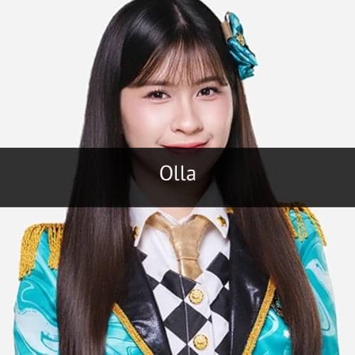 Seorang anggota grup idola mengenakan kostum panggung berwarna biru dan emas dengan dasi emas serta pita di rambutnya.