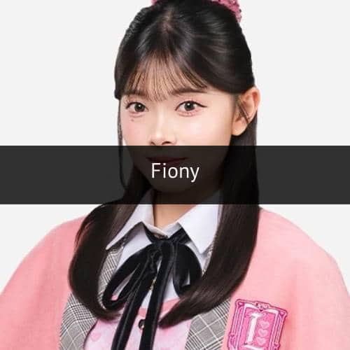 Seorang perempuan berambut panjang mengenakan seragam berwarna pink dan abu-abu dengan pita hitam di leher serta latar belakang putih.