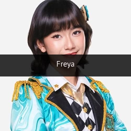 Seorang perempuan berambut pendek mengenakan kostum panggung berwarna biru toska dengan hiasan emas dan dasi bermotif kotak hitam putih.