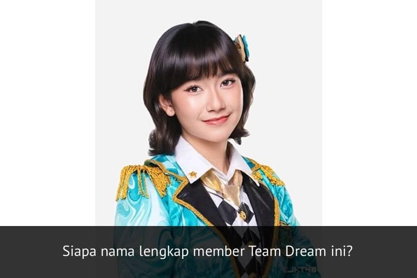Seorang anggota JKT48 Team Dream mengenakan kostum panggung berwarna biru toska dengan aksen emas dan dasi emas, tersenyum ke arah kamera.