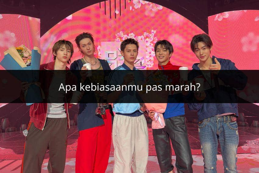 Lima pria muda berdiri di atas panggung dengan latar merah muda, memegang buket bunga dan minuman sambil berpose bersama.