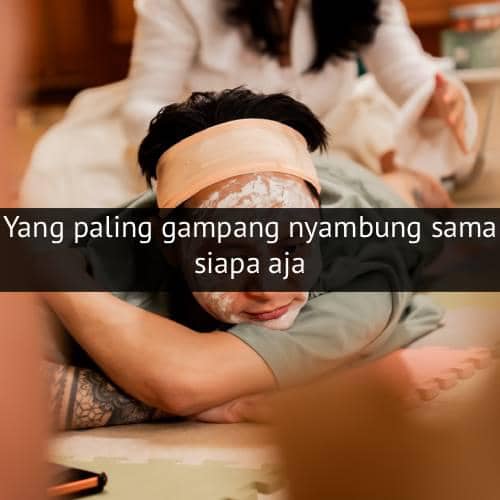 Seseorang berbaring santai dengan masker wajah dan handuk di kepala, sementara orang lain tampak berada di latar belakang.