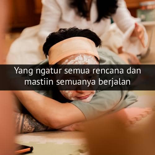 Seseorang berbaring santai dengan masker wajah dan handuk di kepala, sementara orang lain tampak merawatnya di latar belakang.