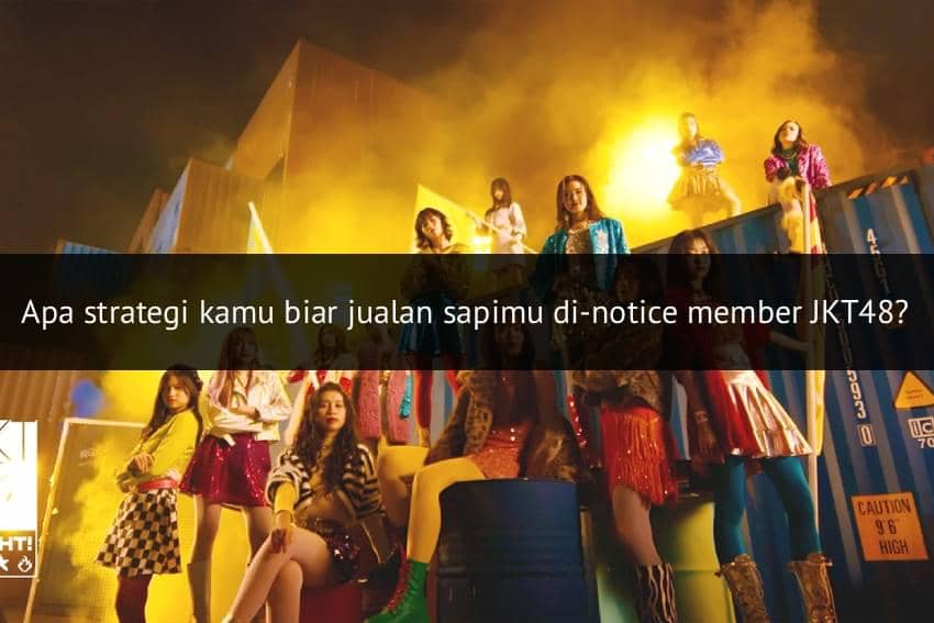 Grup idola JKT48 Team Dream berpose di atas dan sekitar kontainer berwarna biru dengan pencahayaan kuning terang di latar belakang.
