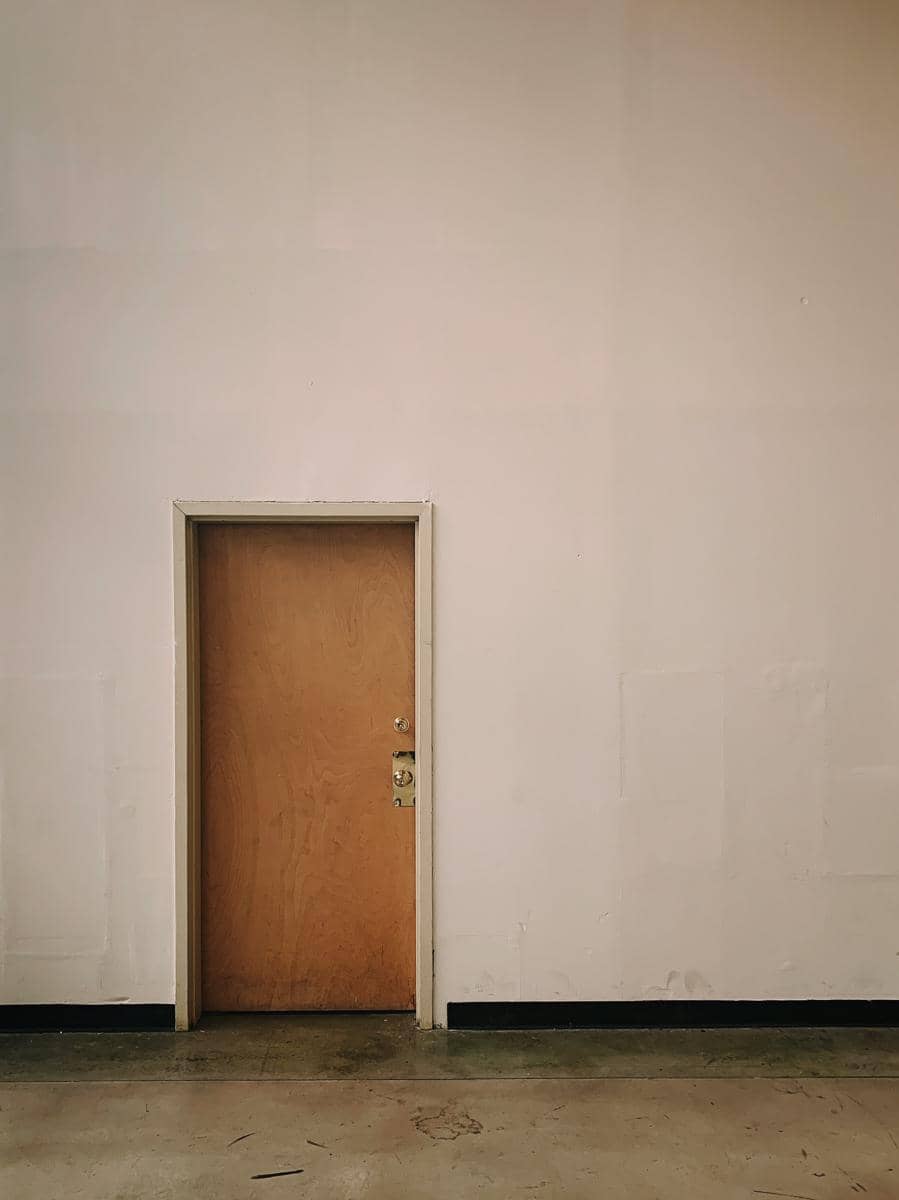 Sebuah pintu kayu dengan dinding putih yang luas dan kosong.