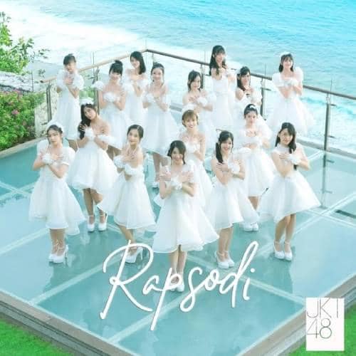 Belasan anggota JKT48 mengenakan gaun putih berpose di atas lantai kaca dengan latar laut biru dan tulisan Rapsodi di bagian depan.