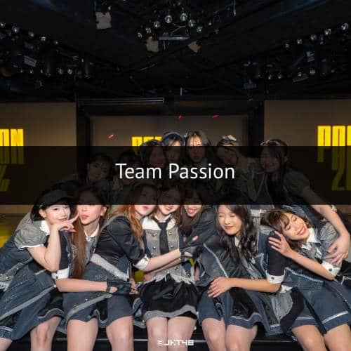 Beberapa anggota grup idola perempuan berpose bersama di atas panggung dengan latar bertuliskan Team Passion.