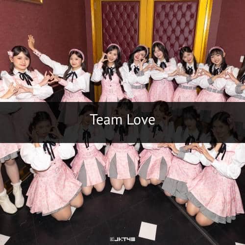 Grup idola wanita mengenakan kostum panggung berwarna merah muda dan putih berpose bersama di depan dinding berwarna merah marun.