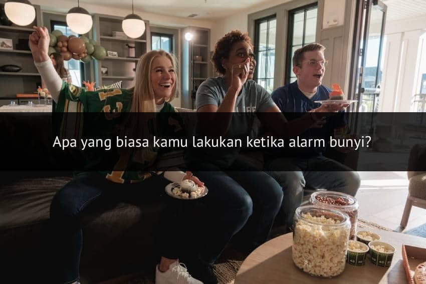 Tiga orang duduk di sofa sambil menonton pertandingan sepak bola di televisi, menikmati camilan popcorn dan bersorak gembira.