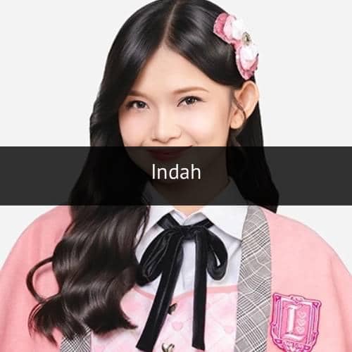Seorang anggota grup idola mengenakan seragam berwarna merah muda dengan pita hitam dan aksesori rambut berbentuk pita.