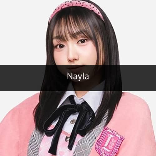 Seorang anggota grup idola mengenakan seragam berwarna pink dan abu-abu dengan pita hitam serta bando pink di rambutnya.