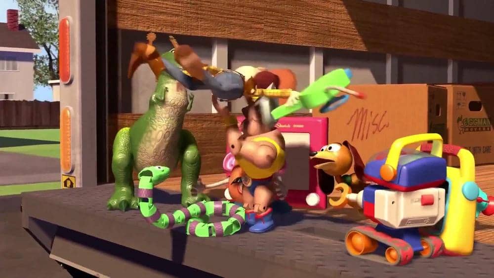 Beberapa mainan karakter animasi dari film Toy Story berdiri di atas truk pindahan dengan latar kotak kardus dan rumah di kejauhan.