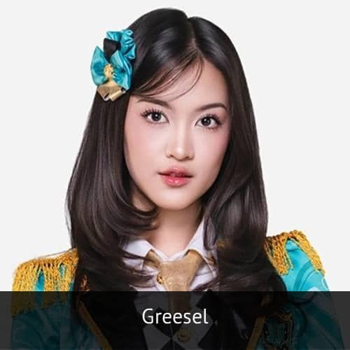 Seorang anggota JKT48 mengenakan seragam panggung berwarna biru dan emas dengan pita rambut senada, berpose di latar belakang putih.