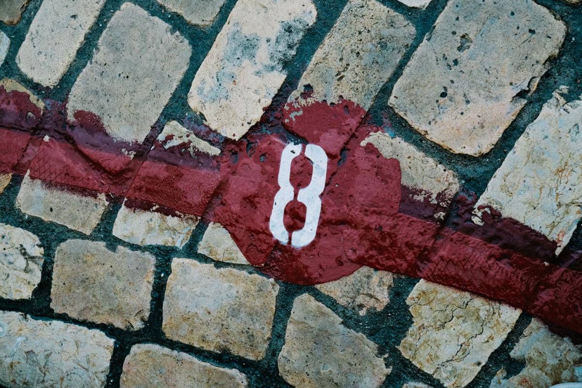 Nomor 8 berwarna putih terlukis di atas jalan berbatu dengan garis merah melintang di permukaannya.