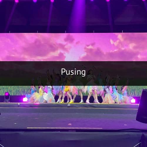 Penampilan grup idola wanita di atas panggung dengan latar layar besar berwarna ungu dan pencahayaan panggung terang.