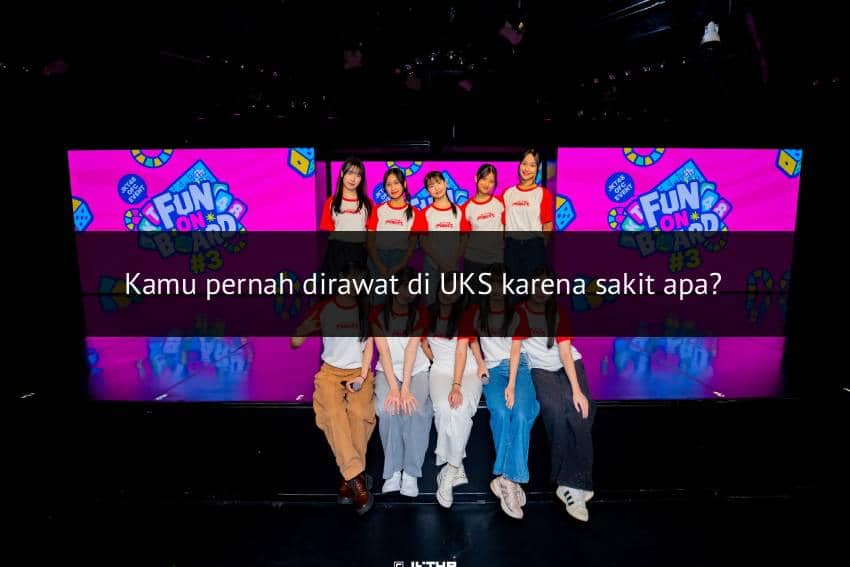 Beberapa anggota grup idola perempuan berpose di depan layar besar berwarna cerah bertuliskan Fun On Road dengan latar panggung hitam.